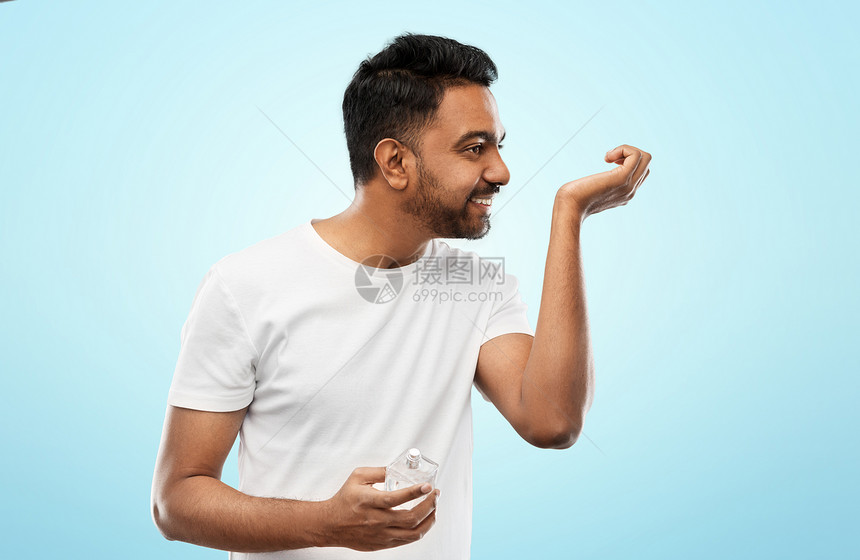 男香水,美容人们的快乐的微笑轻印度男子闻香水蓝色背景快乐的印度男人用蓝色背景的香水图片