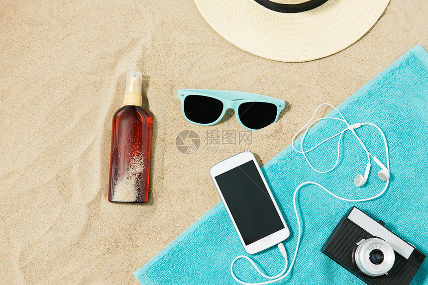 假期暑假智能手机与耳机胶卷相机毛巾,草帽,太阳镜瓶防晒油海滩沙子海滩上的智能手机相机毛巾帽子墨镜图片