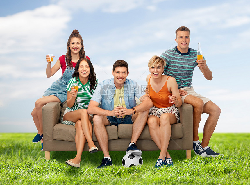娱乐活动休闲人的群快乐的微笑的朋友足球迷,带着足球坐沙发上,蓝天草地背景上喝含酒精的饮料朋友球迷带球饮图片
