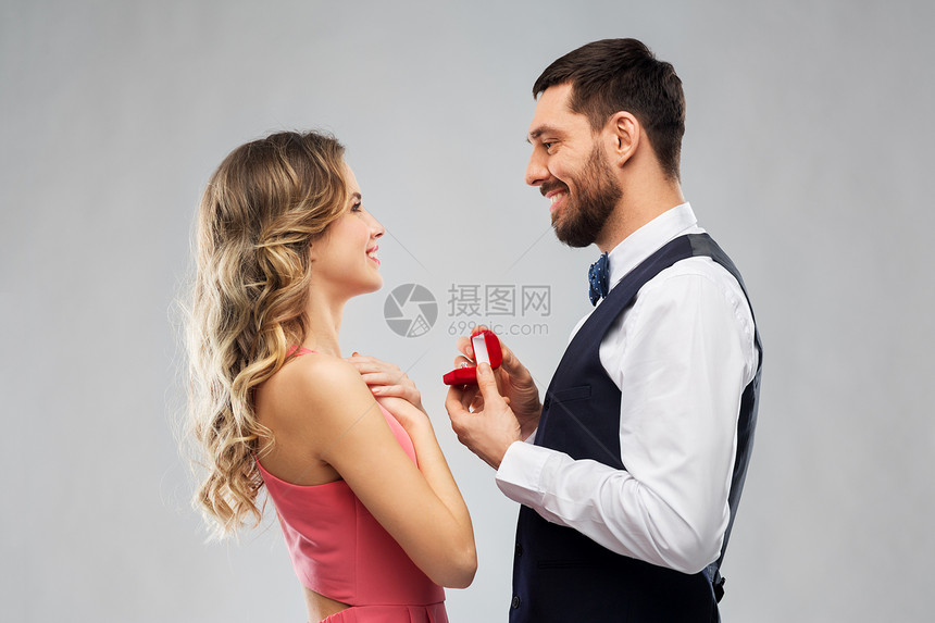 爱情,夫妻,求婚人的快乐的男人给灰色背景的女人小红盒子里的钻石订婚戒指男人情人节给女人订婚戒指图片