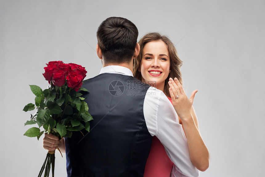 爱情,夫妻,求婚人的快乐的女人与订婚戒指玫瑰拥抱男人灰色的背景女人带着订婚戒指玫瑰拥抱男人图片