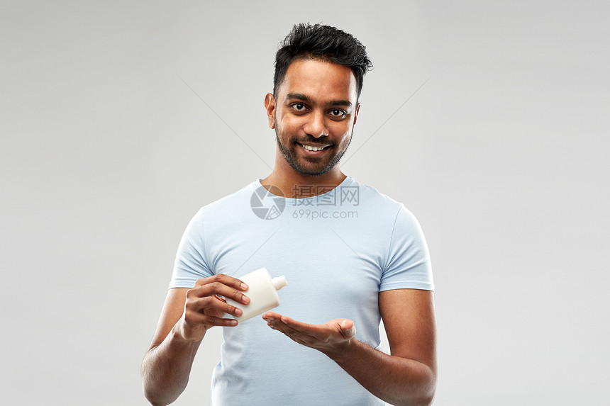 美容,皮肤护理人的微笑的轻印度男子应用乳液他的手灰色的背景快乐的印度男人把乳液涂他的手上图片
