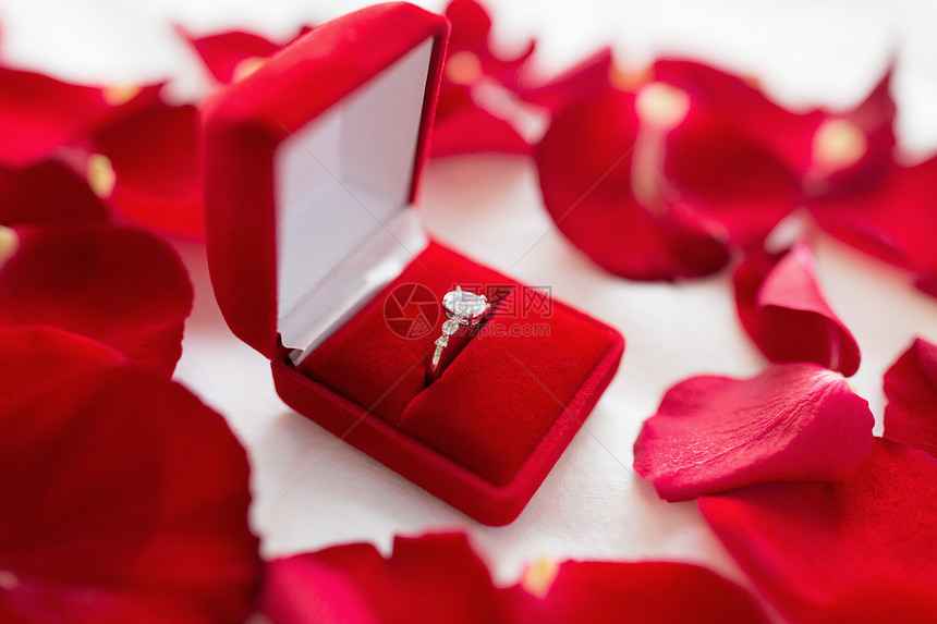 珠宝,求婚浪漫的钻石戒指红色天鹅绒礼品盒床单玫瑰花瓣床单上红色天鹅绒礼品盒里的钻石戒指图片