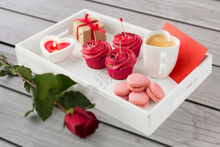 情人节糖果纸杯蛋糕与红色奶油霜心形鸡尾酒棒,马卡龙,蜡烛,咖啡杯礼品盒托盘上情人节的红色糖果背景图片