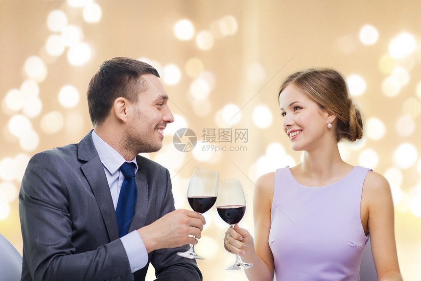 约会庆祝情人节的微笑的轻夫妇碰杯含酒精的红酒,并米色背景上的节日灯上看着其他餐厅轻的夫妇餐厅喝了杯图片