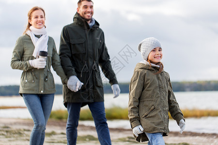 家庭休闲人的快乐的母亲父亲小女儿沿着秋天的海滩散步幸福的家庭沿着秋天的海滩散步背景图片