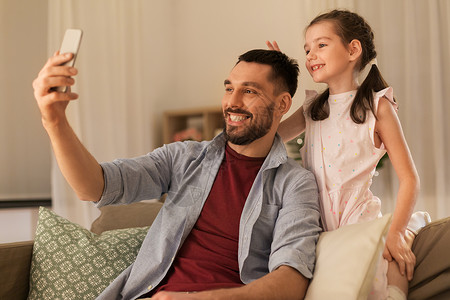 人,家庭技术快乐的父亲小女儿家里用智能手机自拍父亲女儿家自拍图片
