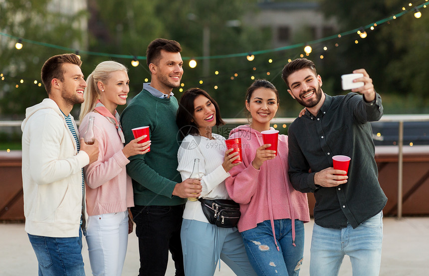 休闲人们的快乐的朋友聚会杯里喝饮料,夏天用智能手机屋顶上自拍饮料的朋友屋顶派上自拍图片