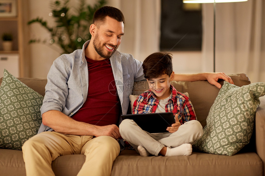 家庭,父亲,技术人的快乐的父亲小儿子与平板电脑电脑坐家里的沙发上父子俩家里玩平板电脑图片