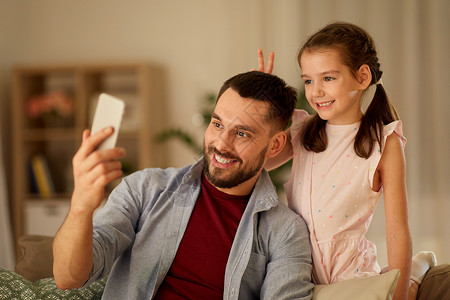 人,家庭技术快乐的父亲小女儿家里用智能手机自拍父亲女儿家自拍图片