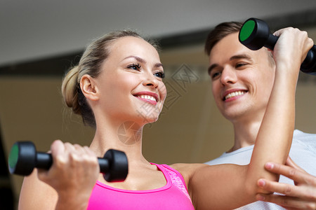 运动,健身人的微笑的女人与私人教练哑铃健身房锻炼哑铃的女人健身房锻炼图片