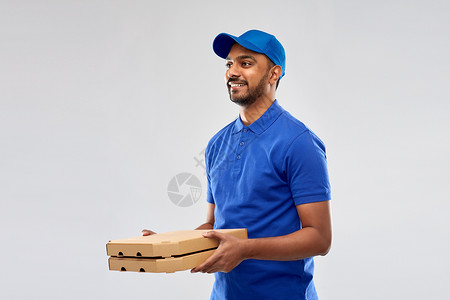 服务人的快乐的印度送货人与比萨饼盒蓝色制服灰色背景快乐的印度送货人带着蓝色的披萨盒背景图片