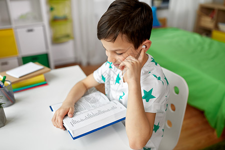 词汇书教育,童技术快乐的学生男孩耳机阅读书籍学外语家里学生男孩戴着耳机家看书背景