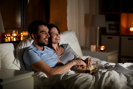 微笑舒适度人,家庭休闲夫妇与爆米花晚上家看电视夫妇晚上家看电视吃爆米花背景