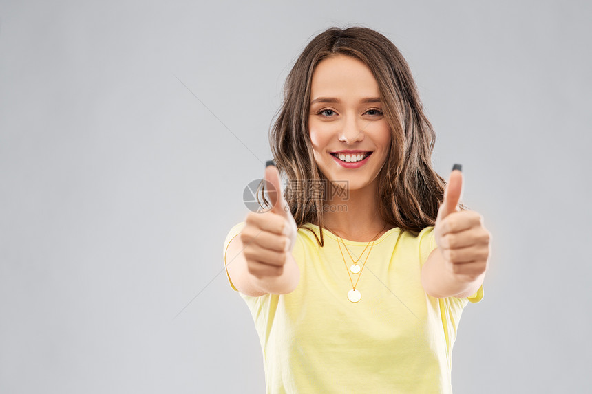 手势人的微笑的轻女人十几岁的女孩穿着空白的黄色T恤,灰色背景上竖大拇指轻的女人十几岁的女孩竖大拇指图片