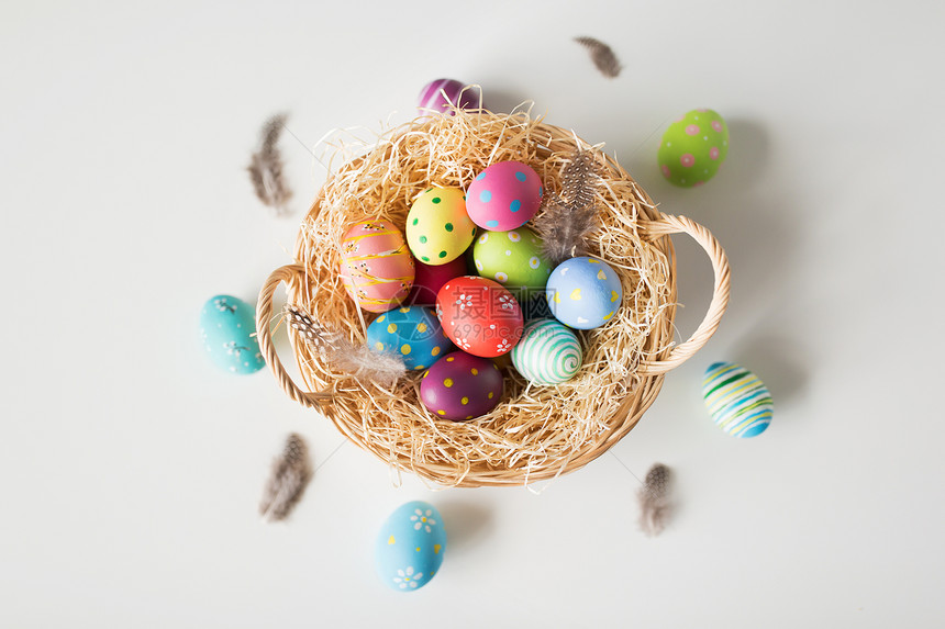 复活节,假日传统彩色鸡蛋篮子与稻草鹌鹑羽毛白色背景篮子里的彩色复活节彩蛋图片