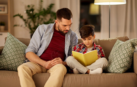 家庭童父爱休闲人的父亲小儿子晚上家沙发上看书父子家看书沙发图片
