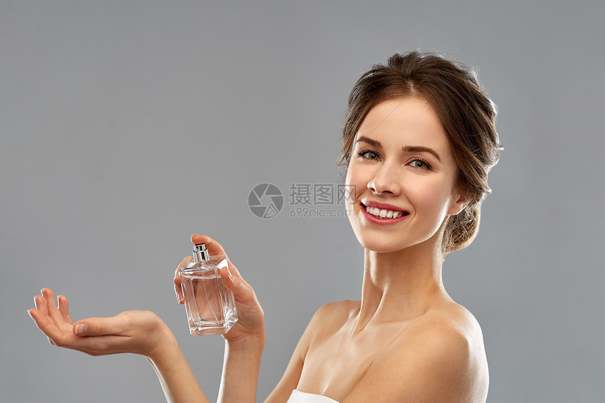 香水,美丽奢侈的快乐的微笑轻女子喷洒香水她的手腕灰色的背景带着灰色背景的香水的快乐女人图片