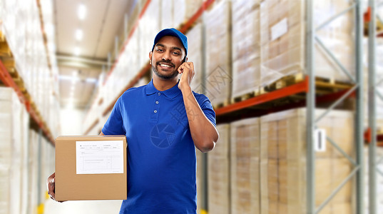 邮件服务,沟通装运快乐的印度送货人员仓库工人与智能手机包裹箱蓝色制服货物背景送货人仓库智能手机盒子背景图片