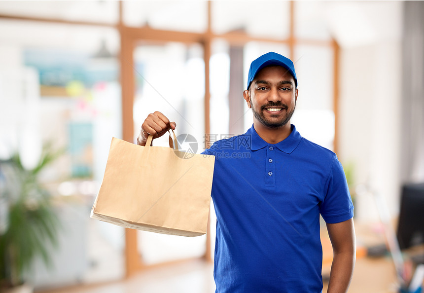 外卖服务人的快乐的印度送货人食品纸袋蓝色制服办公室背景送货人办公室用纸袋送食物图片