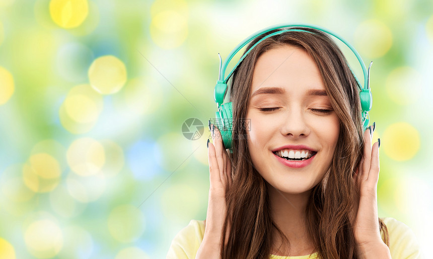 音乐,技术人的快乐的轻女人十几岁的女孩戴着耳机夏天的绿灯背景下带耳机的快乐的轻女人十几岁的女孩图片