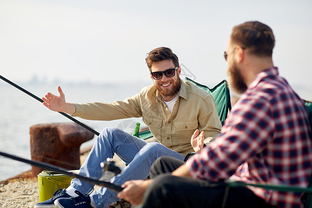 休闲人的快乐的男朋友与杆码头上的海上讲述捕鱼的故事快乐的男朋友与棒谈论钓鱼背景图片