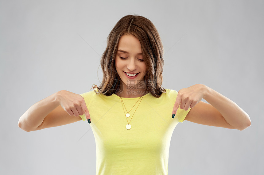 人们的微笑的轻女人十几岁的女孩穿着空白的黄色T恤,手指向下指向灰色背景穿黄色T恤的轻女人少女图片