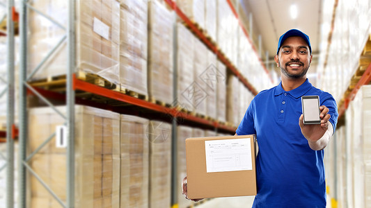 邮件服务,技术装运快乐的印度送货人员仓库工人与智能手机包裹箱蓝色制服货物背景送货人仓库智能手机盒子背景图片