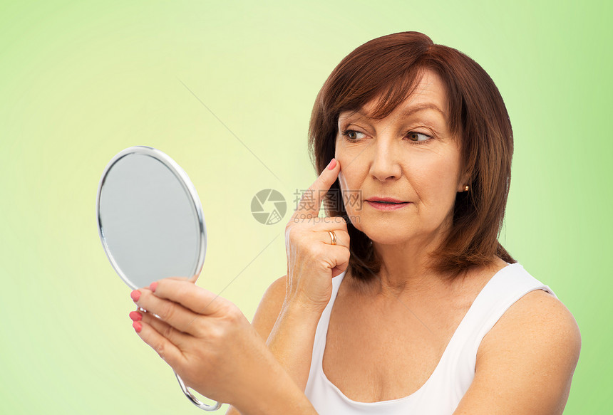 老年女人对着镜子触摸她的脸颊图片