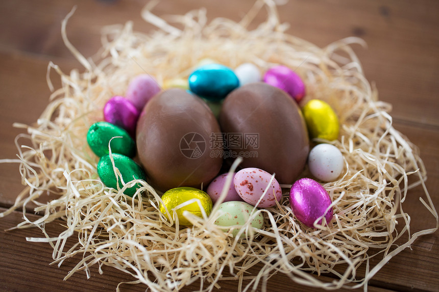 复活节,糖果假日巧克力鸡蛋箔纸包装稻草窝木桌上稻草巢箔包装纸中的巧克力蛋图片