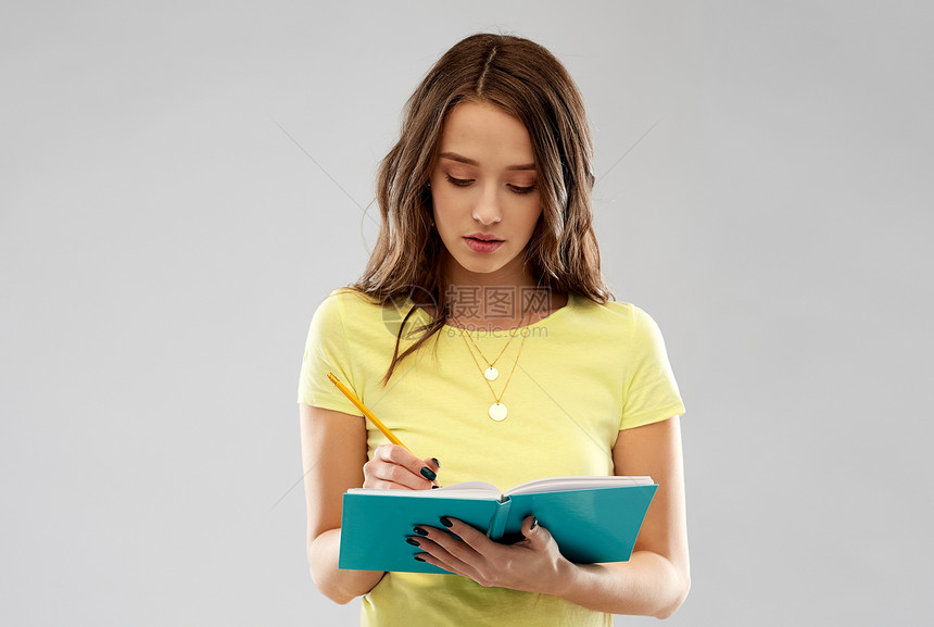 教育,学校,灵感人的轻的妇女十几岁的学生女孩穿黄色T恤,用铅笔灰色背景上写日记笔记本十几岁的学生女孩写日记图片