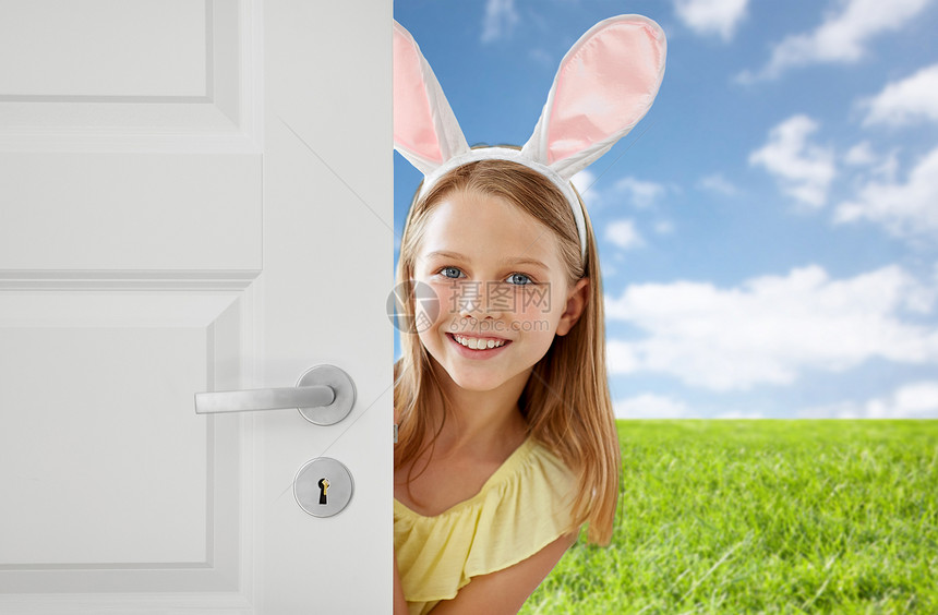 复活节,假日人们的快乐的女孩戴着兔子的耳朵,蓝天草地背景上窥视着门外快乐的女孩,复活节兔子的耳朵偷看门外图片