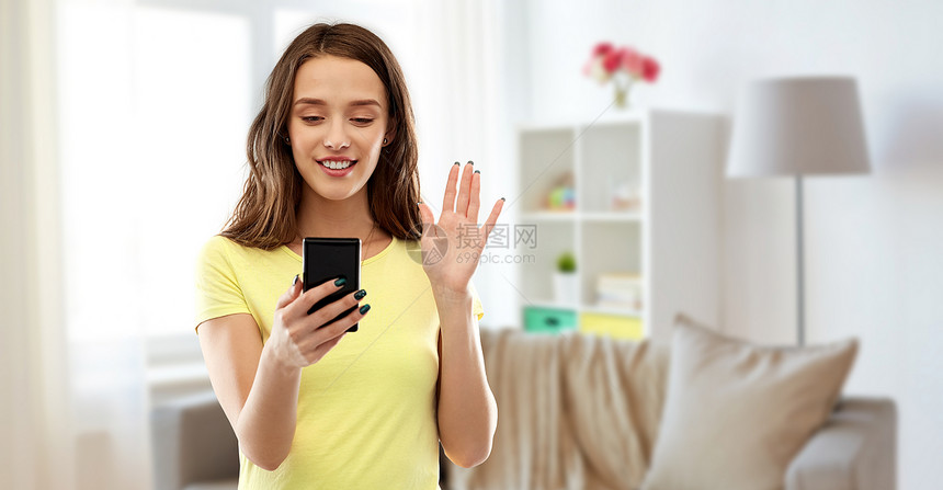 技术人的微笑的轻妇女十几岁的女孩穿着空白的黄色T恤,家庭客厅背景上视频呼叫智能手机微笑的十几岁女孩视频呼叫图片