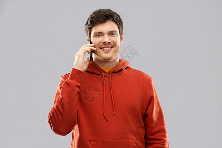 技术,沟通人的微笑的轻人穿着红色帽衫,灰色背景下打电话给智能手机穿着红色帽衫的轻人打电话给智能手机背景图片
