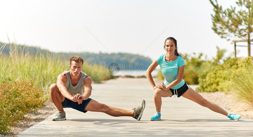健身,运动生活方式的微笑夫妇伸展腿海滩上训练前微笑的情侣海滩上伸展腿图片