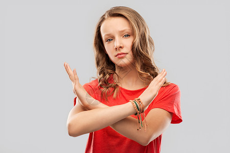 责难禁止人的严肃的少女灰色背景上表现出交叉的手禁止的手势十几岁的女孩用令人讨厌的手势交叉双手背景