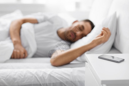 床头柜手机技术人的智能手机床头柜附近的轻人睡家里的床上床头柜上的智能手机靠近熟睡的男人背景