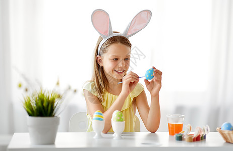 兔子与女孩复活节,假日人们的快乐的女孩戴着兔子耳朵,头带着色鸡蛋与颜色刷子家里快乐的女孩家里给复活节彩蛋着色背景