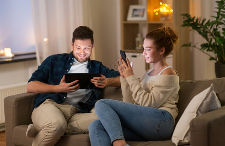 微笑舒适度休闲,技术网络成瘾的快乐的夫妇与平板电脑智能手机家里晚上家里平板电脑智能手机设计图片