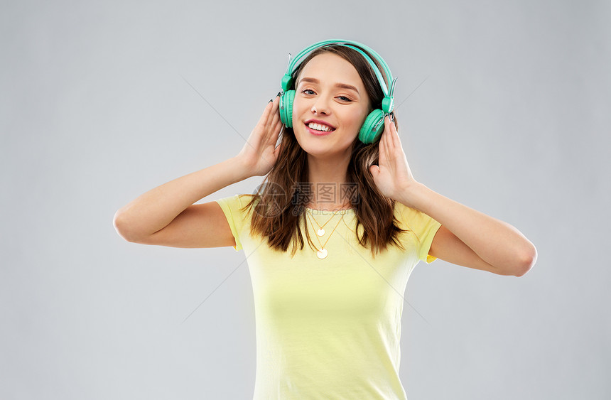 音乐,技术人的快乐的轻女人十几岁的女孩戴着灰色背景的耳机带耳机的快乐的轻女人十几岁的女孩图片