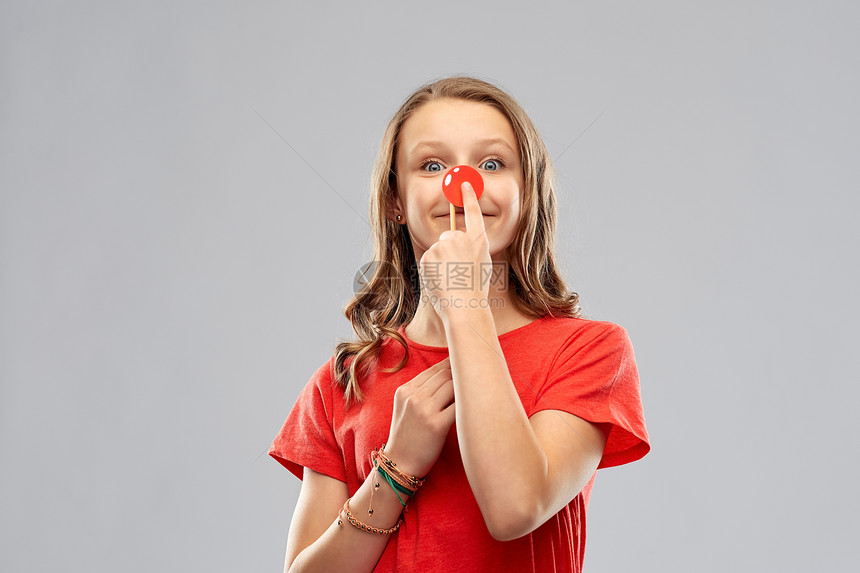红鼻子日,慈善人们的微笑的十几岁女孩T恤与小丑鼻子灰色背景带着红色小丑鼻子的微笑的十几岁女孩图片