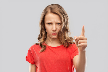 警告,注意力人的愤怒的皱眉少女指着灰色的背景愤怒的皱着眉头的十几岁女孩竖手指背景图片