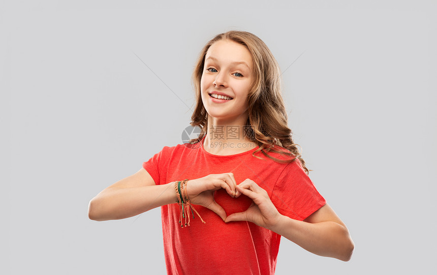 情人节,爱慈善微笑的十几岁女孩,留着长发,穿着红色T恤,灰色背景上手势微笑的十几岁女孩穿着红色的手心图片