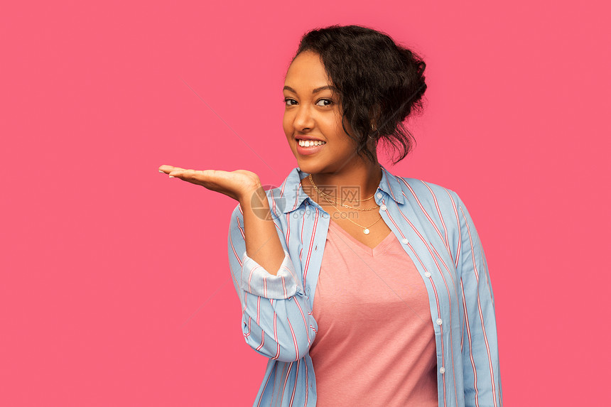 人广告快乐的非裔美国轻女人着些想象的东西空着手粉红色的背景快乐的非洲女人手里着东西图片