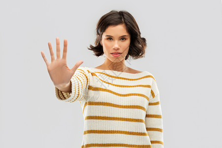 限制,禁止人的轻妇女穿条纹套头衫,灰色背景上停止手势轻的女人着停止的手势图片
