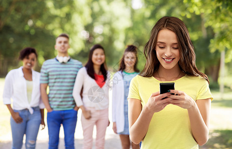 技术人的微笑的轻妇女十几岁的女孩穿着空白的黄色T恤,用智能手机群朋友的夏季公园背景用智能手机的轻女背景