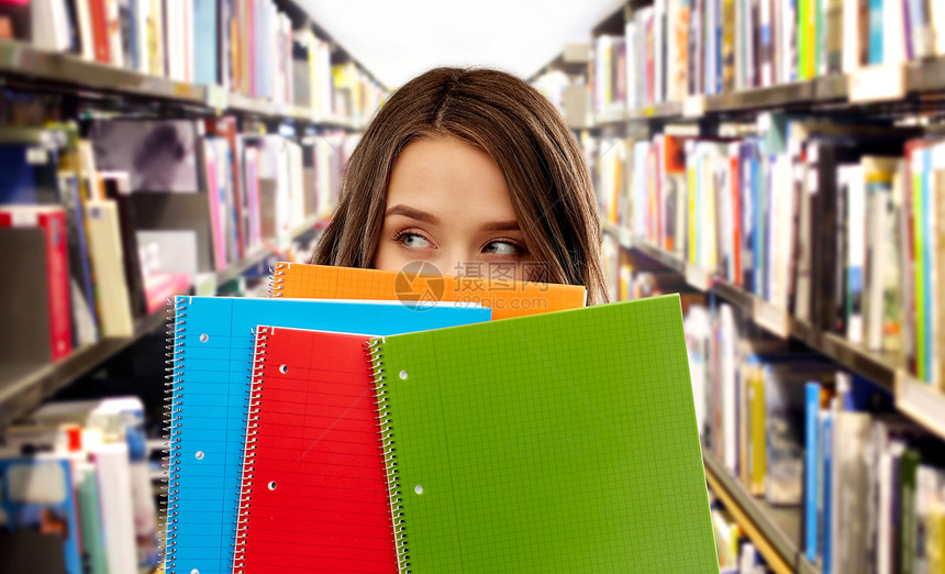 教育学校知识轻妇女十几岁的学生女孩躲图书馆背景的书架上的笔记本后图书馆笔记本后的十几岁的学生女孩图片