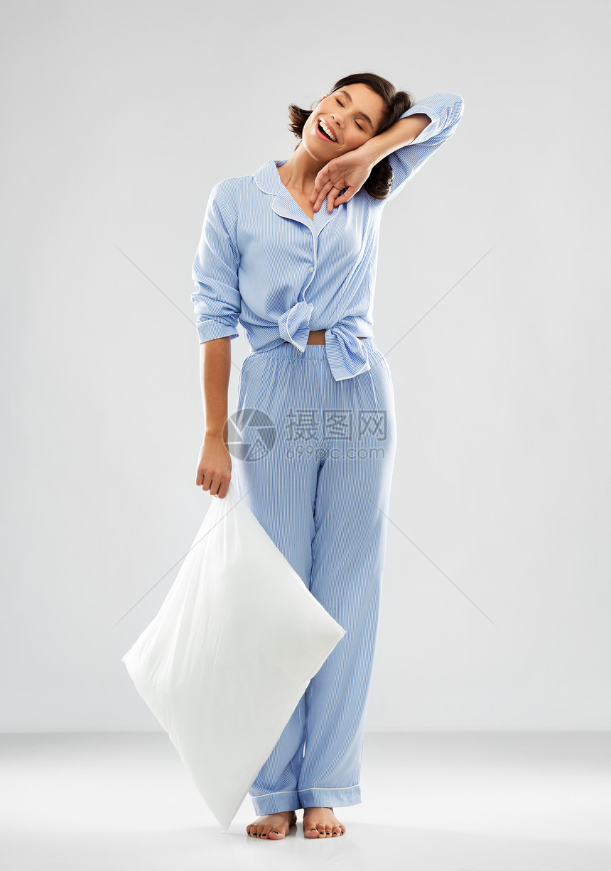 人们睡觉时间的快乐困倦的轻女人蓝色睡衣抱着枕头灰色的背景快乐困倦的女人穿着蓝色睡衣抱着枕头图片