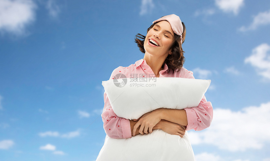人们睡前的快乐的轻女人睡衣眼罩拥抱枕头蓝天云彩的背景戴着睡衣枕头眼罩的女人图片