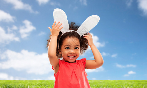 兔子头童,派道具复活节快乐的非裔美国女孩戴着兔子耳朵头巾蓝天草地背景快乐的小女孩戴着复活节兔子的耳朵背景